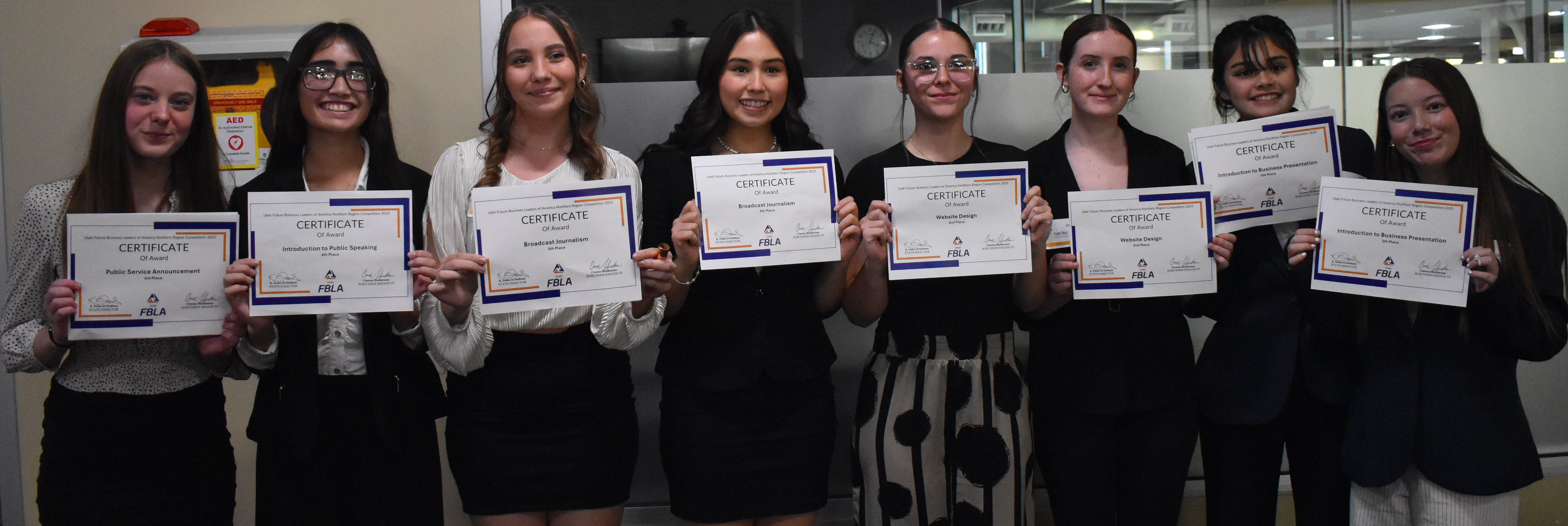 A group of eight students proudly pose indoors, each holding up a certificate of achievement.